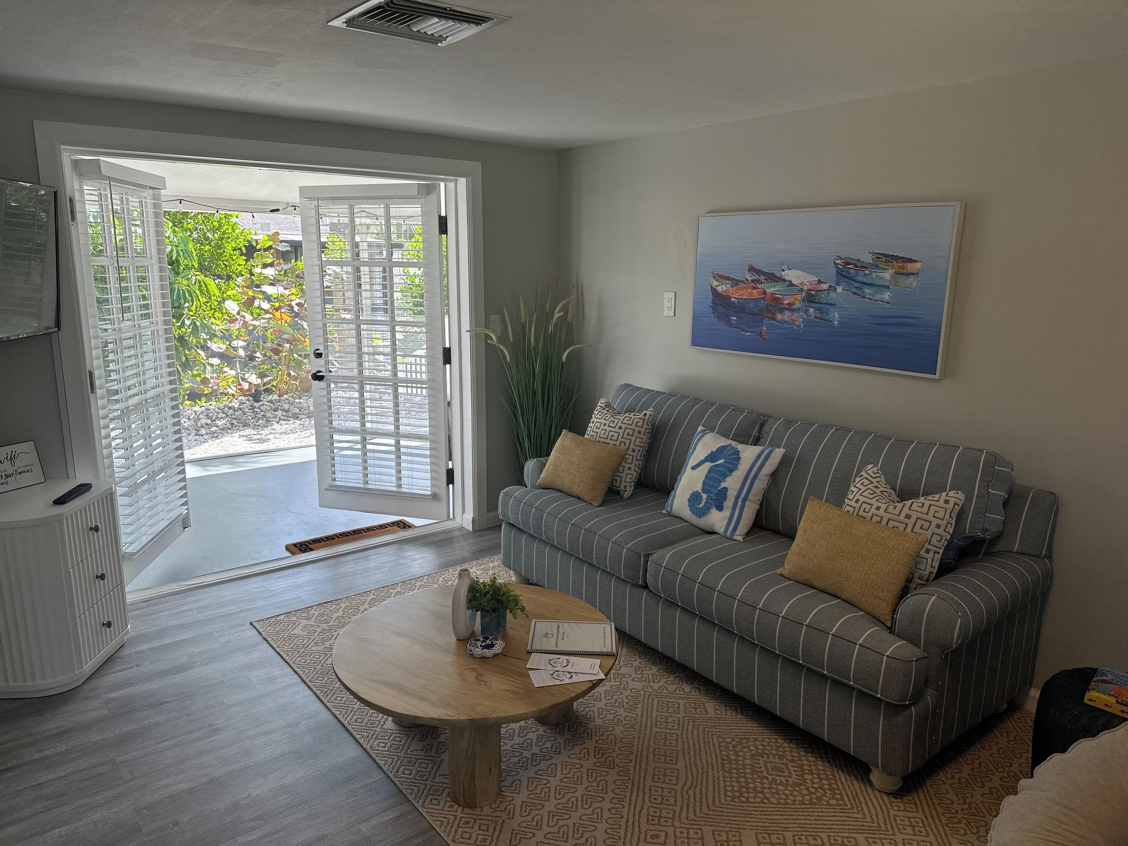 A living room with a grey-striped sofa, a coffee table, and a painting of boats on water.