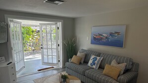 A living room with a grey-striped sofa, a coffee table, and a painting of boats on water. - Seashell Serenity Beach Escape - Just 5 minutes from Lovely Bonita Beach Park! (Bonita Springs)