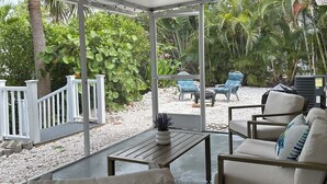A covered patio area with a wooden table, two white cushioned chairs, and a sofa. - Seashell Serenity Beach Escape - Just 5 minutes from Lovely Bonita Beach Park! (Bonita Springs)