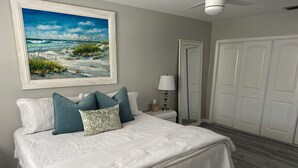 A bedroom with a bed, pillows, a nightstand, a lamp, a mirror, and a wardrobe. - Seashell Serenity Beach Escape - Just 5 minutes from Lovely Bonita Beach Park! (Bonita Springs)