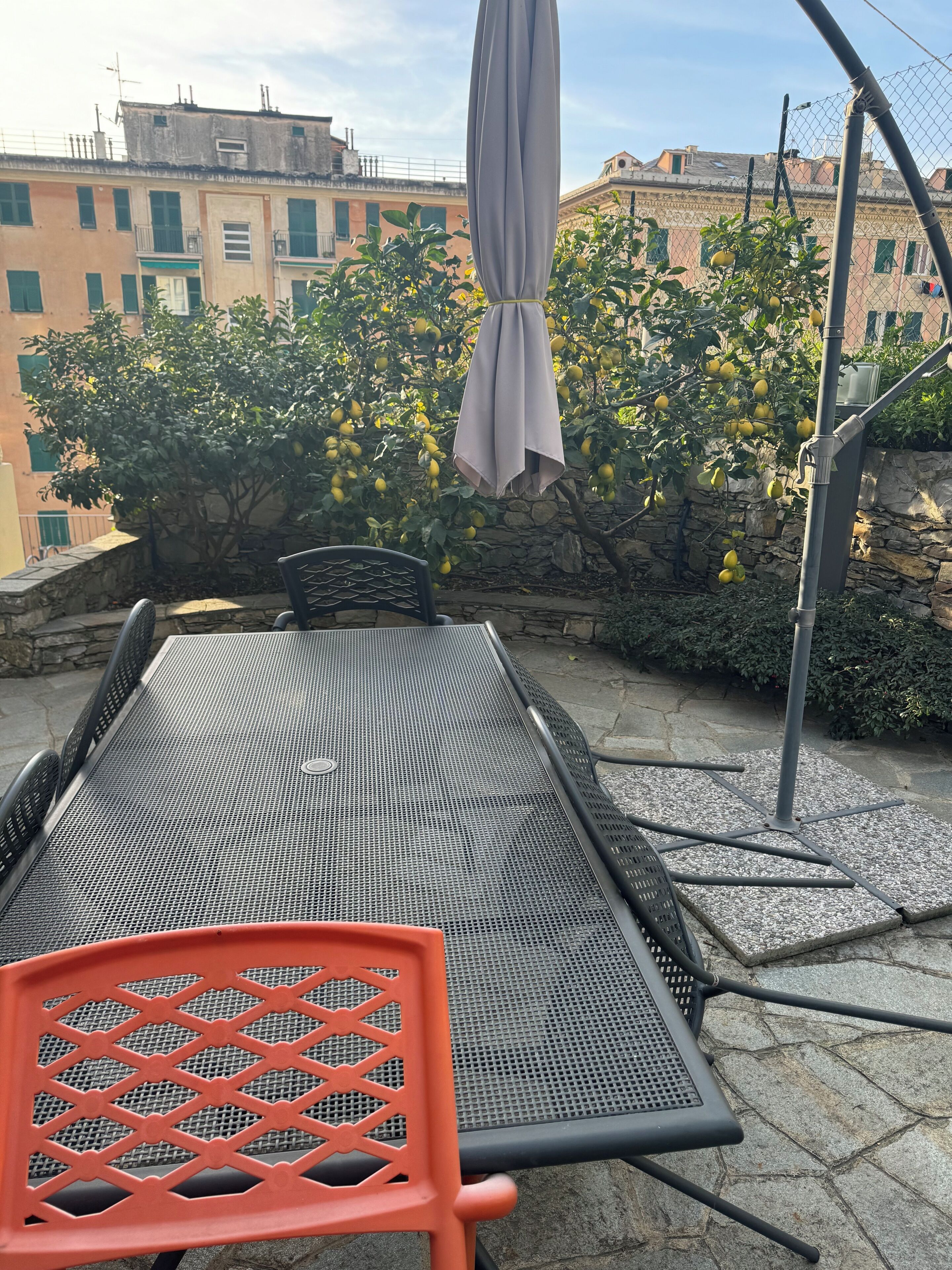 An outdoor patio with a metal table and chairs, a hanging umbrella, and a stone wall with a lemon tree.