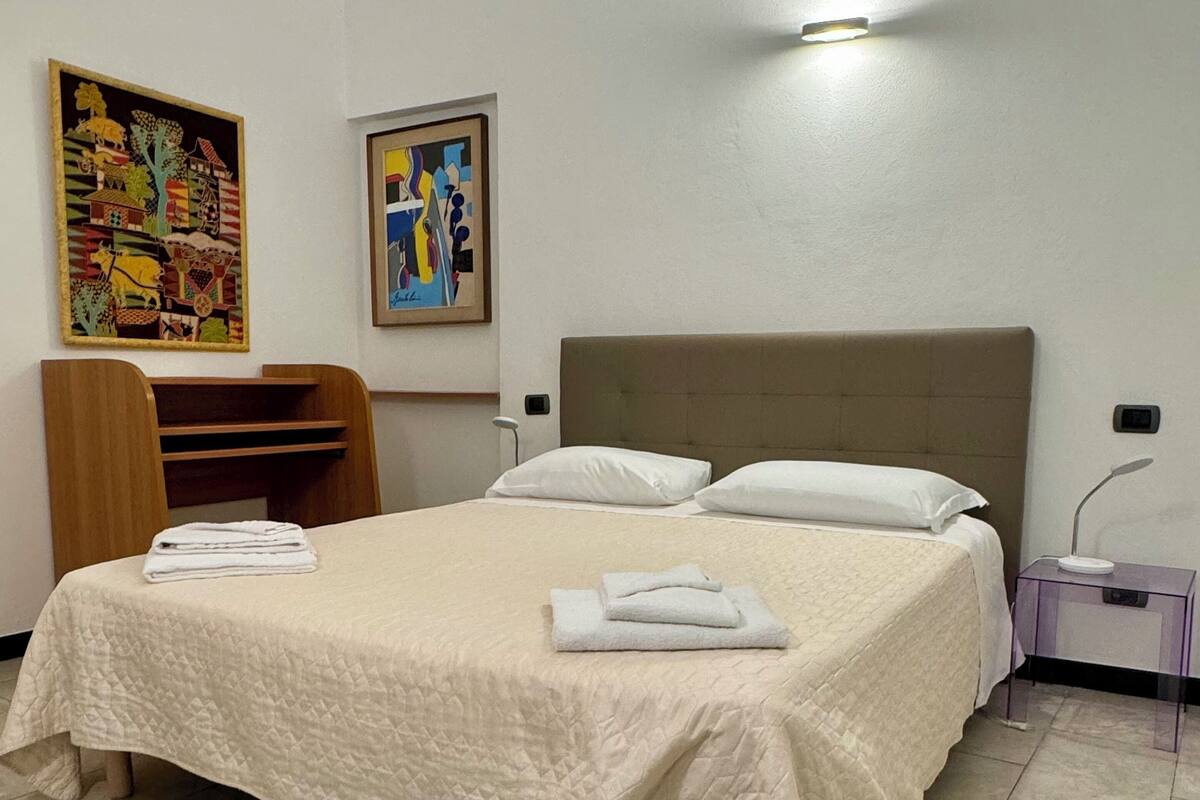 Une chambre d’hôtel avec un lit de taille « queen », une chaise en bois, une table de chevet et deux tableaux accrochés au mur.