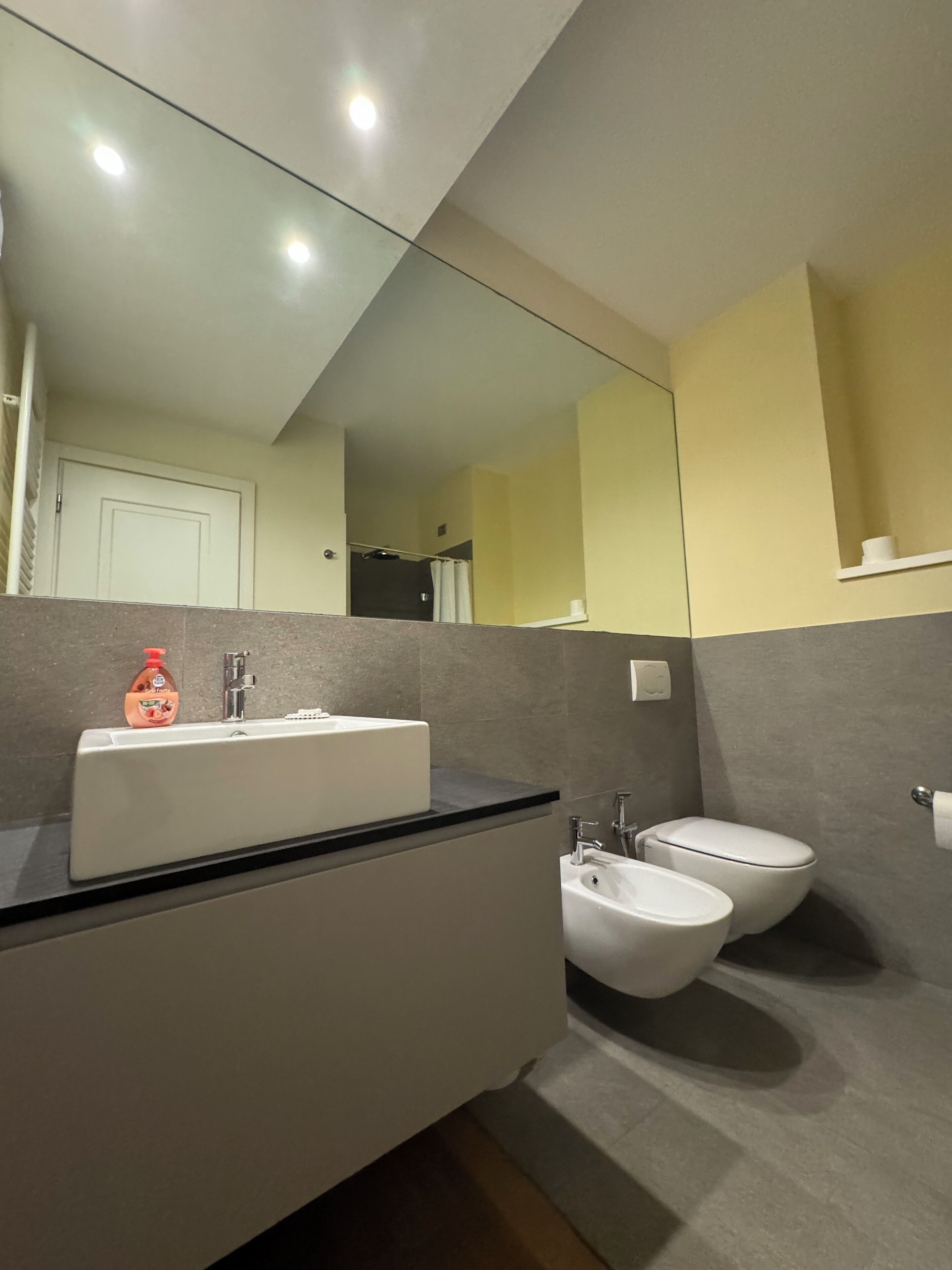 Uma casa de banho moderna com lavatório branco, dois bidés, espelho e sanita.