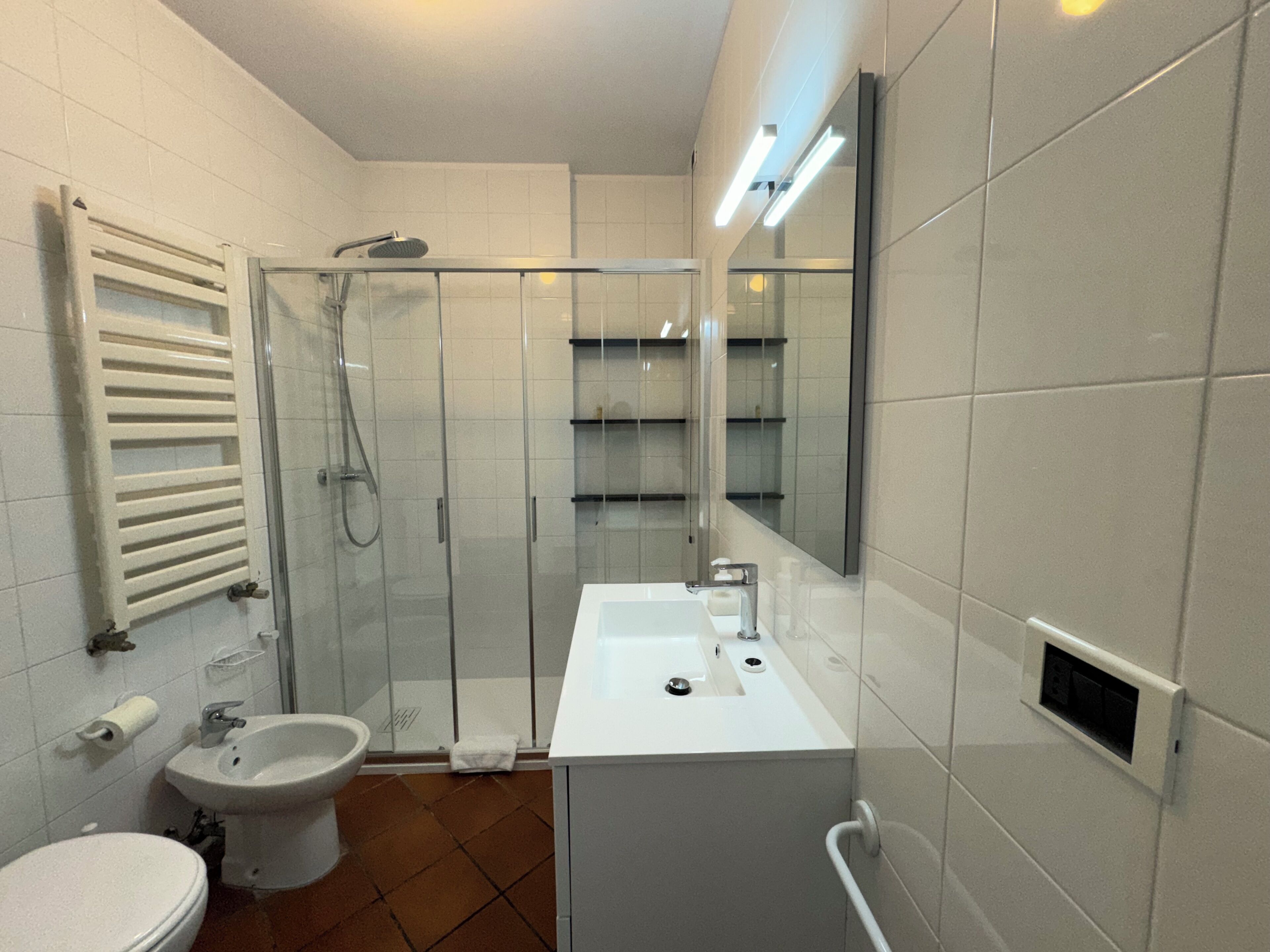 Un bagno moderno con doccia vetro, lavabo bianco e water.