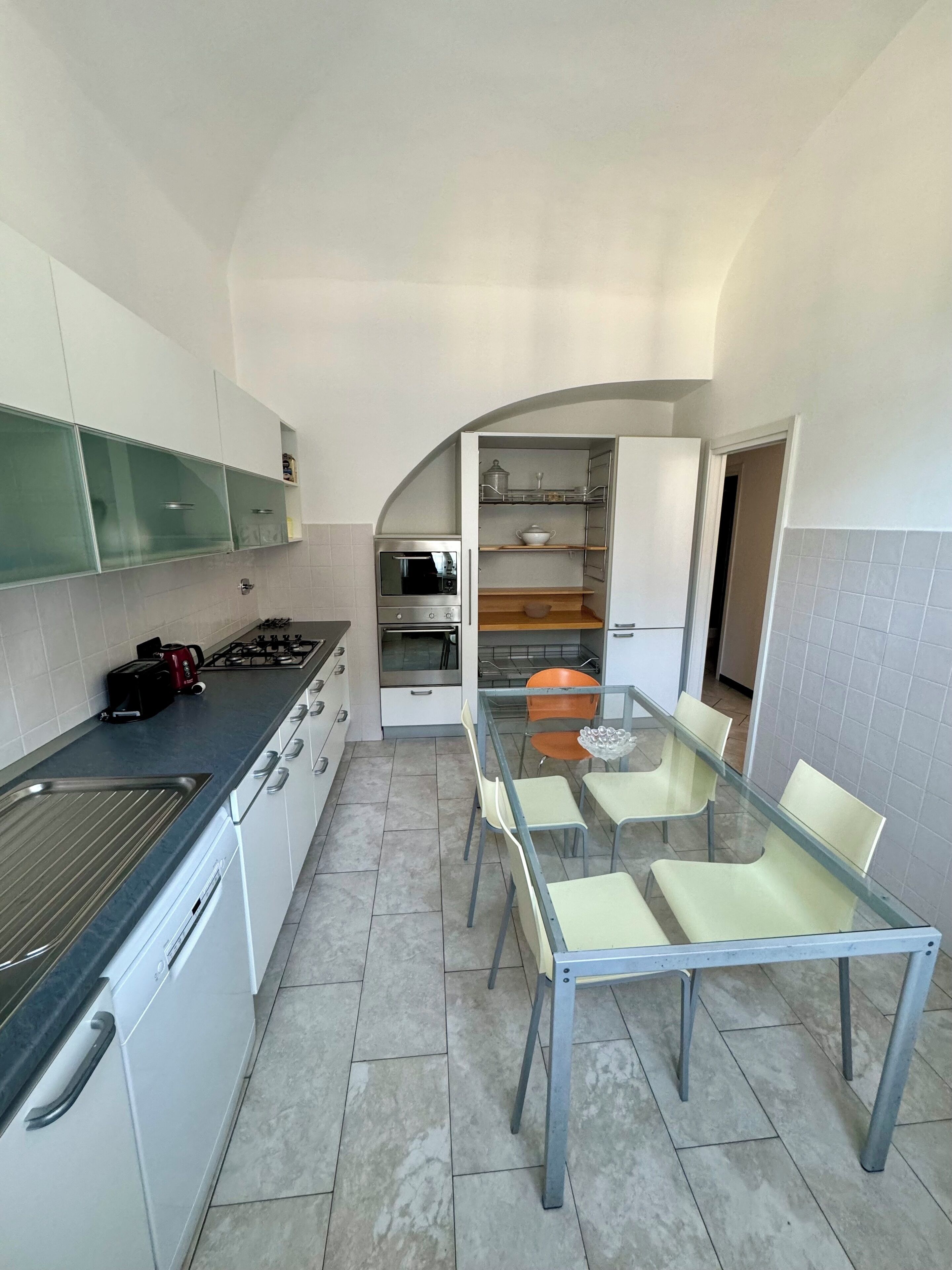 A modern kitchen with white cabinets, a gas stove, an oven, and a dining area with a glass table and chairs.