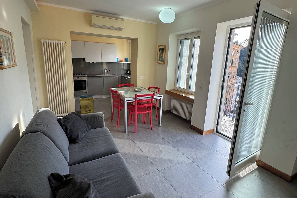 Un salon moderne avec un canapé gris, une table à manger avec des chaises rouges et un coin cuisine doté de meubles blancs et d’une cuisinière.