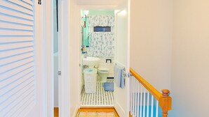 Een gang die leidt naar een badkamer met een houten vloer, witte muren en een gestreept vloerkleed.