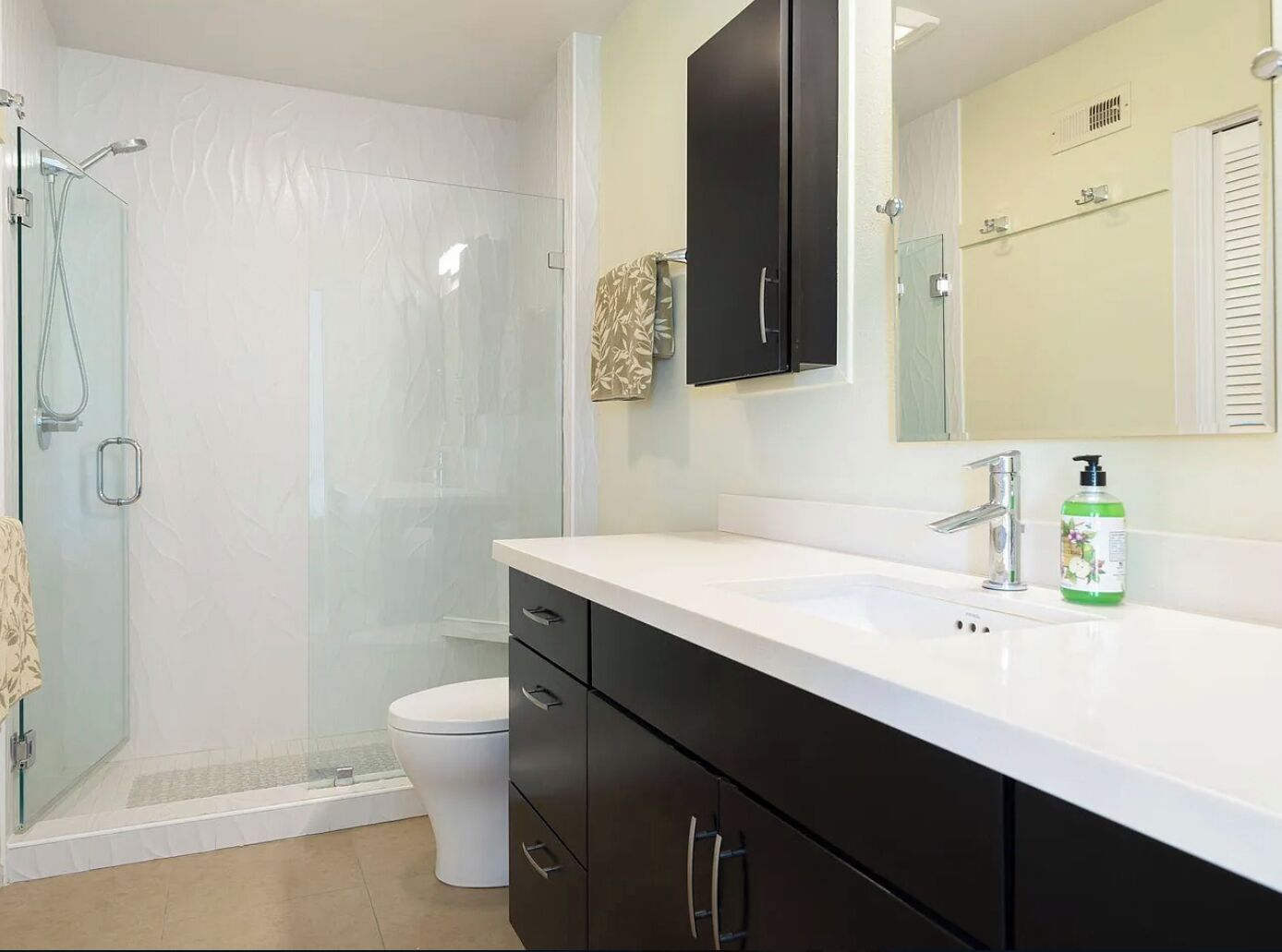 A modern bathroom with a glass shower enclosure, a white toilet, a black vanity with drawers, a white sink, and a mirror above the sink.