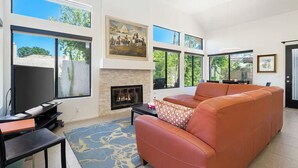 Una sala de estar con chimenea, ventanas amplias, un sofá y un televisor de pantalla plana.