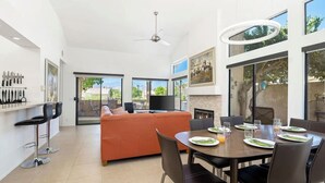 Una sala de estar moderna con comedor, ventanas amplias y ventilador de techo.