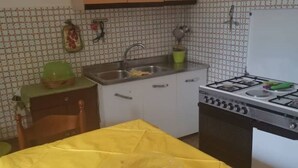 A kitchen with a gas stove, sink, and a yellow tablecloth-covered table. - 🏡 Holiday Apartment in Policastro Bussentino (Policastro Bussentino)
