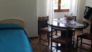 A room with a bed, a round dining table with chairs, a window with curtains, and a small table with a vase of flowers. - 🏡 Holiday Apartment in Policastro Bussentino (Policastro Bussentino)