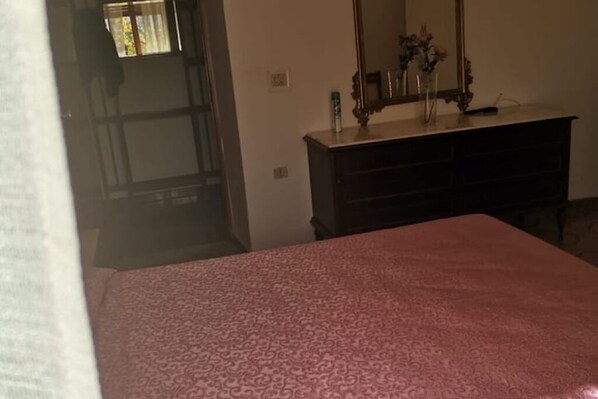 A room with a patterned bedspread, a dresser with a mirror, and a vase with flowers.