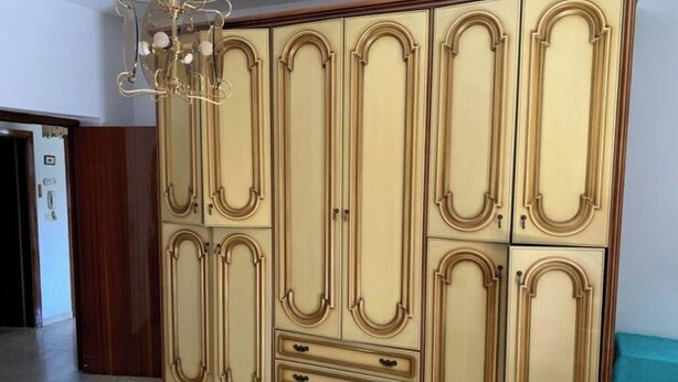 A large, cream-colored wardrobe with multiple doors and drawers, featuring ornate gold detailing and a chandelier above. - 🏖️ Cozy Holiday Apartment 300m from the Sea - Policastro Bussentino #1 (Policastro Bussentino)