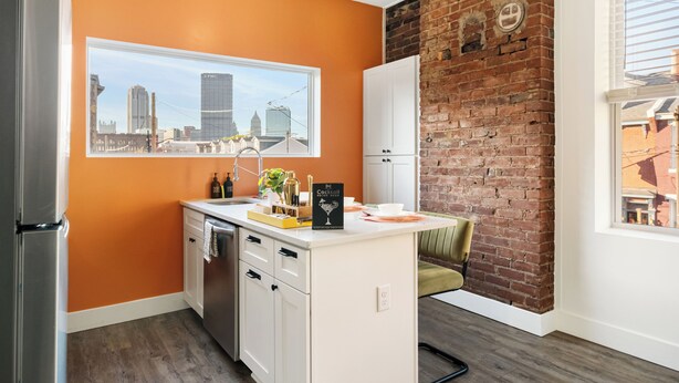 A modern kitchen with a cityscape view, a brick accent wall, and a small island with seating.