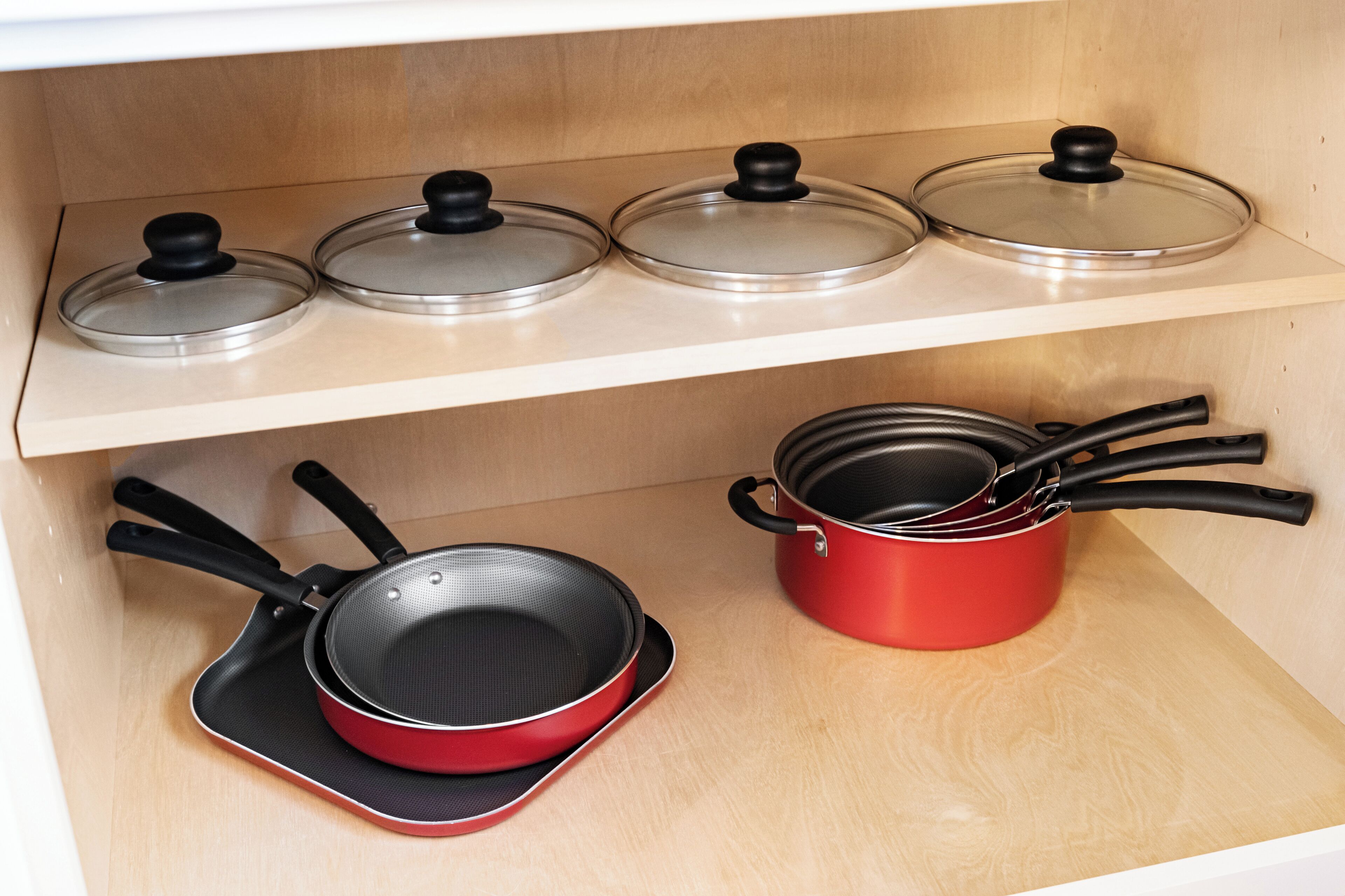 Una cocina con un estante de madera que sostiene cuatro tapas de vidrio y una olla roja con asa negra.