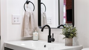 A bathroom with a white sink, black faucet, and a potted plant.