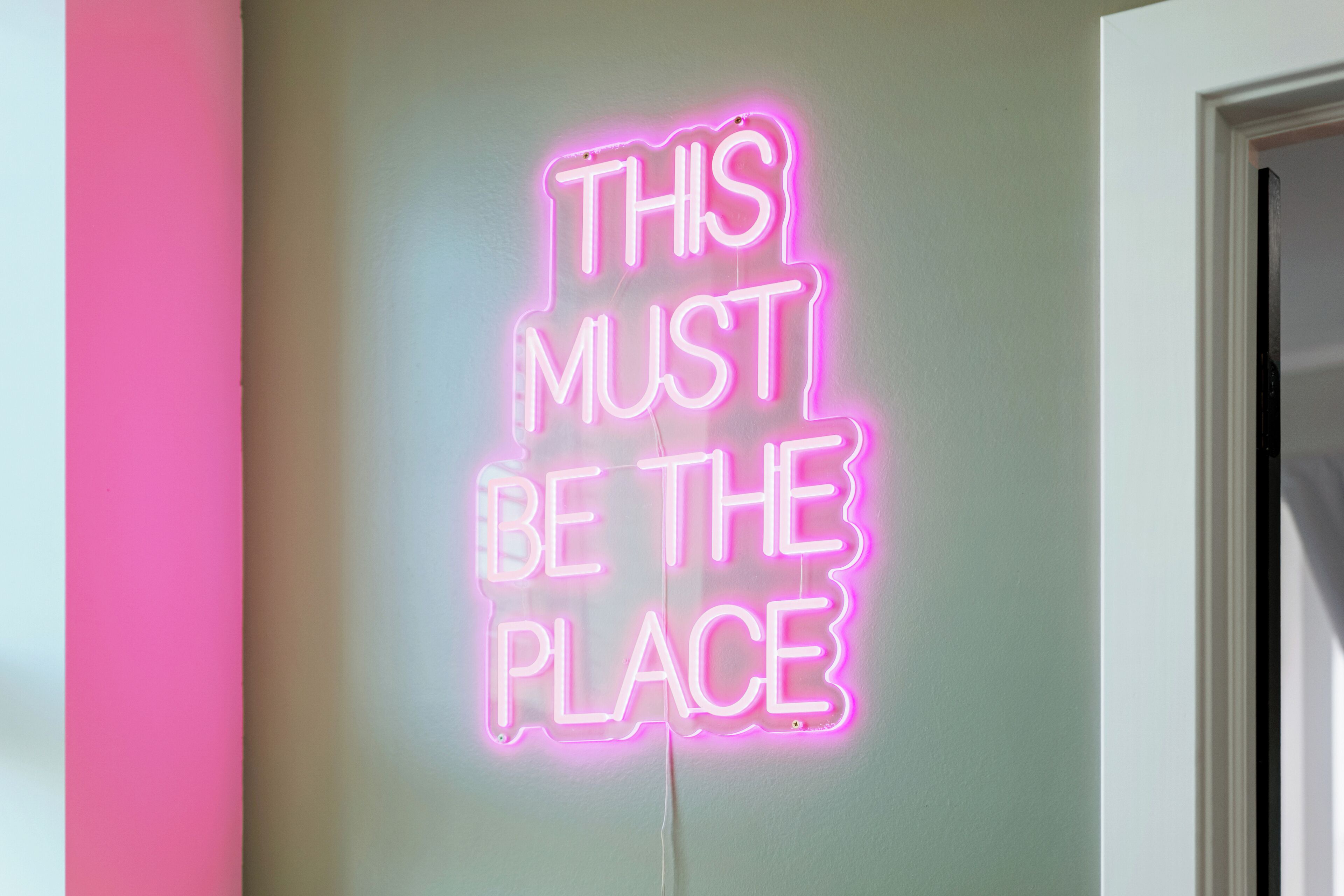 A neon sign with the text "THIS MUST BE THE PLACE" on a wall.