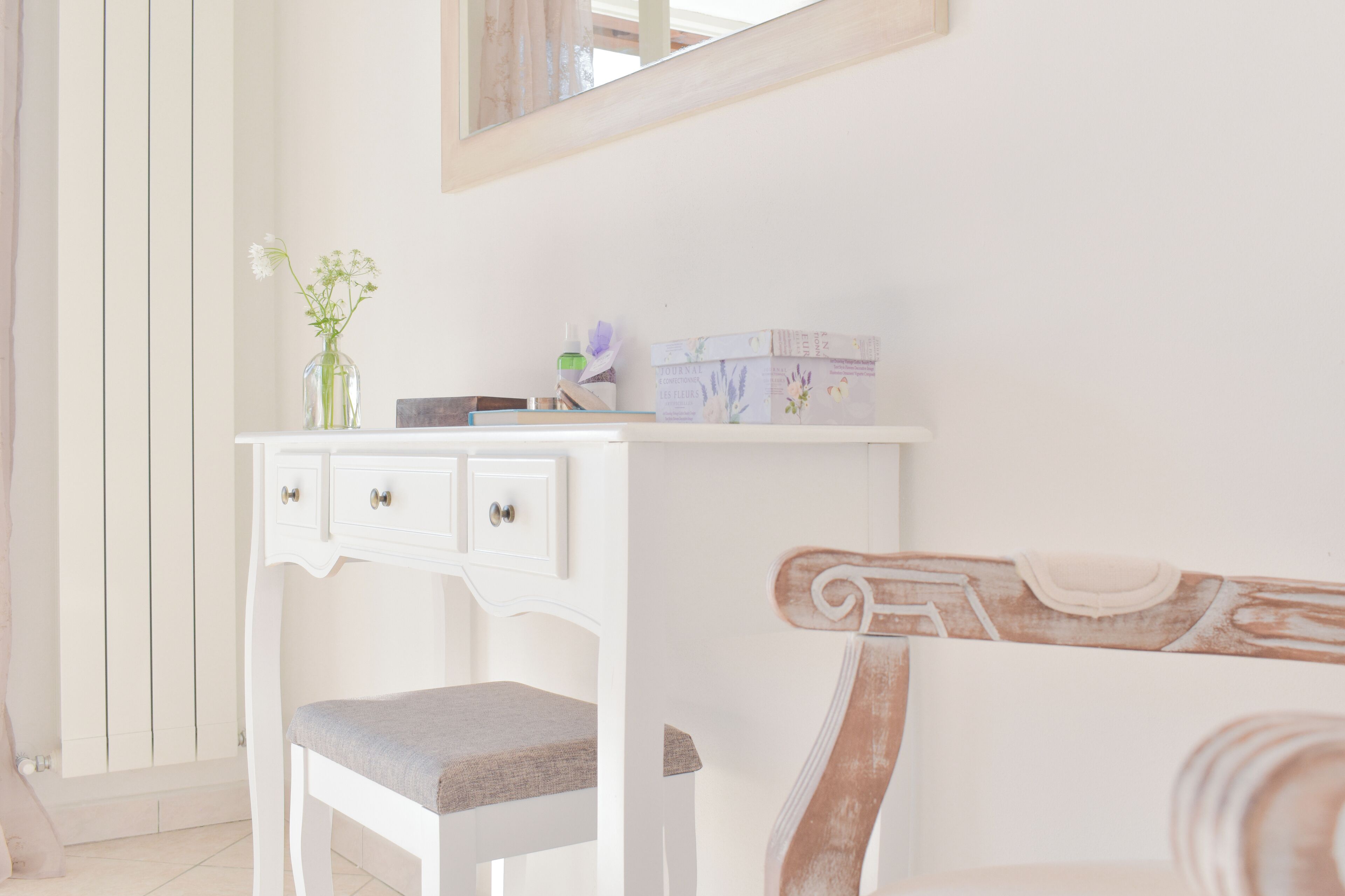 A white vanity with a mirror, a small vase with flowers, and toiletry boxes.