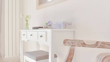 A white vanity with a mirror, a small vase with flowers, and toiletry boxes.