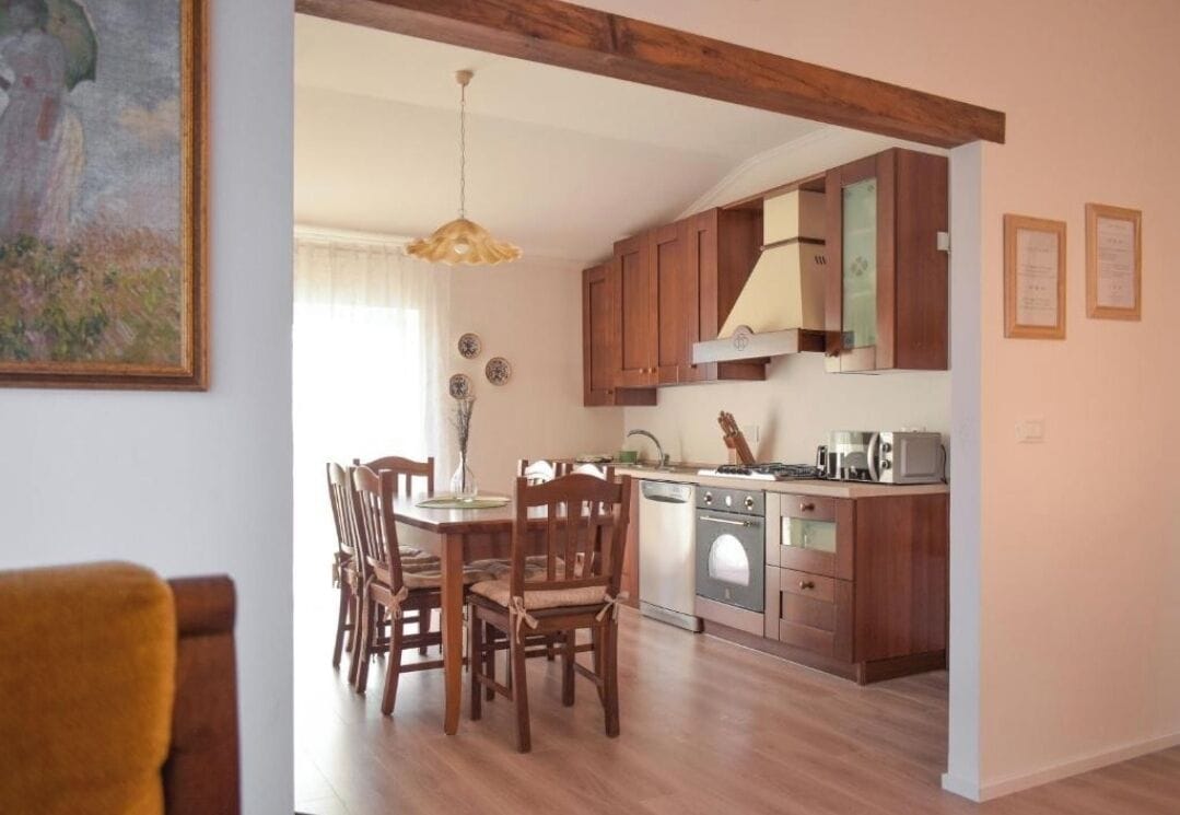 A dining area with wooden chairs and a table, a kitchen with wooden cabinets and appliances, and a painting on the wall.