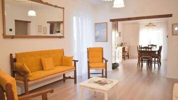 A living room with a sofa, armchair, and a dining area with a table and chairs.