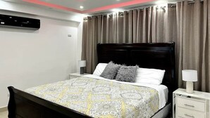 A bedroom with a bed, nightstands, a ceiling fan, curtains, and an air conditioning unit. - Luna by Suarez Properties | Jacuzzi, & BBQ (Santo Domingo Este)