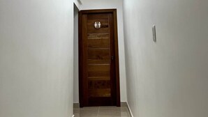 A hallway with a wooden door, white walls, and a ceiling with linear lighting fixtures. - Luna by Suarez Properties | Jacuzzi, & BBQ (Santo Domingo Este)