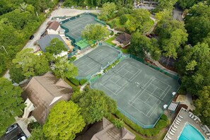 Vista aérea de una propiedad con múltiples canchas de tenis, piscina y vegetación circundante.