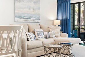 A living room with a sofa, pillows, a table, and a painting of the ocean.