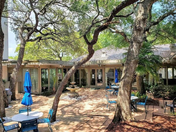 Un patio al aire libre con mesas y sillas, un área de estar techada y una fuente.