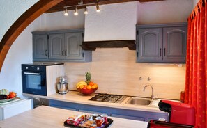 Une cuisine équipée d’une cuisinière à gaz, d’un évier et d’un saladier rempli de fruits posé sur le plan de travail.