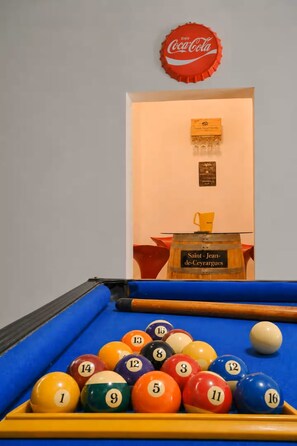 A pool table with a variety of colored balls, a pool cue, and a red Coca-Cola bottle cap on the wall.
