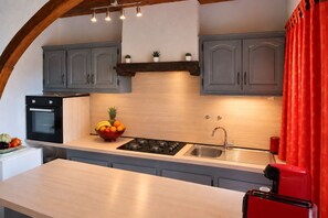 Una cocina con armarios grises, encimera de madera, un electrodoméstico rojo y un frutero.
