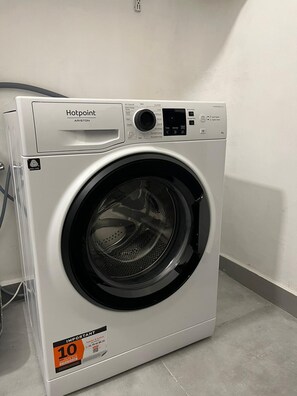 Una lavadora blanca Hotpoint con panel de control, pantalla digital y un adhesivo de descuento de '10'.