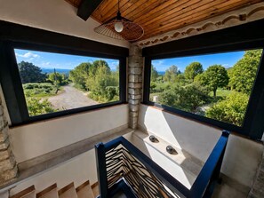 A room with a view of a green landscape through large windows, a stone pillar, and a ceiling fan. - Le Cocon de Soie, charming gîte between Uzès, Nîmes and Anduze, in the Gard . (Saint-Jean-de-Ceyrargues)
