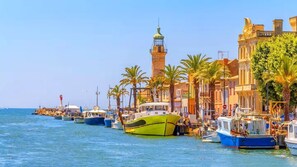 A waterfront with boats docked, a prominent lighthouse, and buildings with classical architecture.