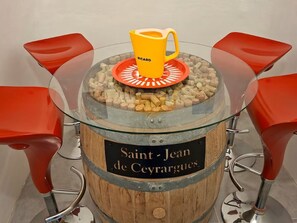 A table with a glass top, surrounded by red chairs, and a wooden barrel with a label reading 'Saint-Jean de Ceyrargues'.
