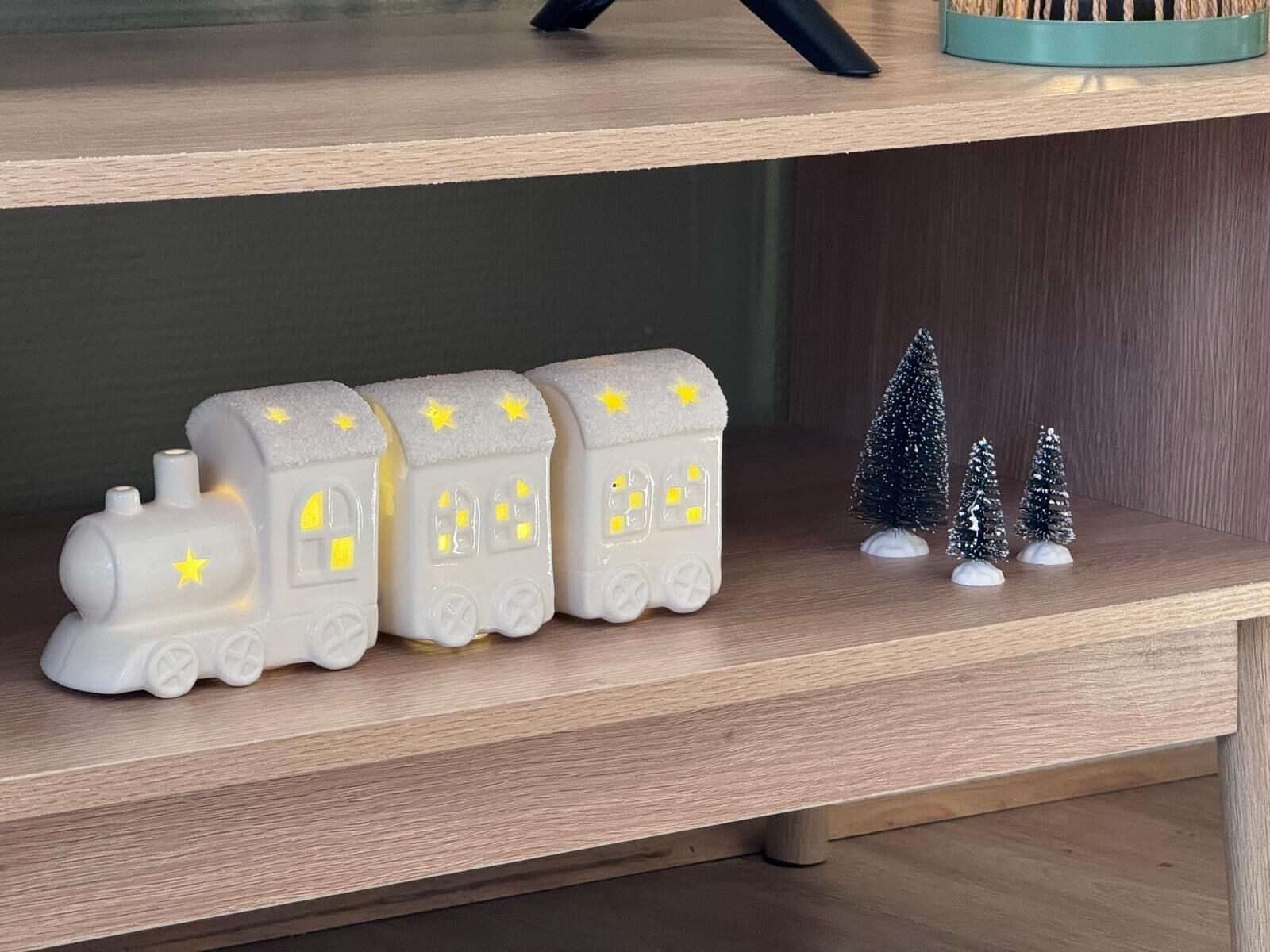 Ein Regal mit drei weißen Modelleisenbahnen und drei kleinen Weihnachtsbäumen.
