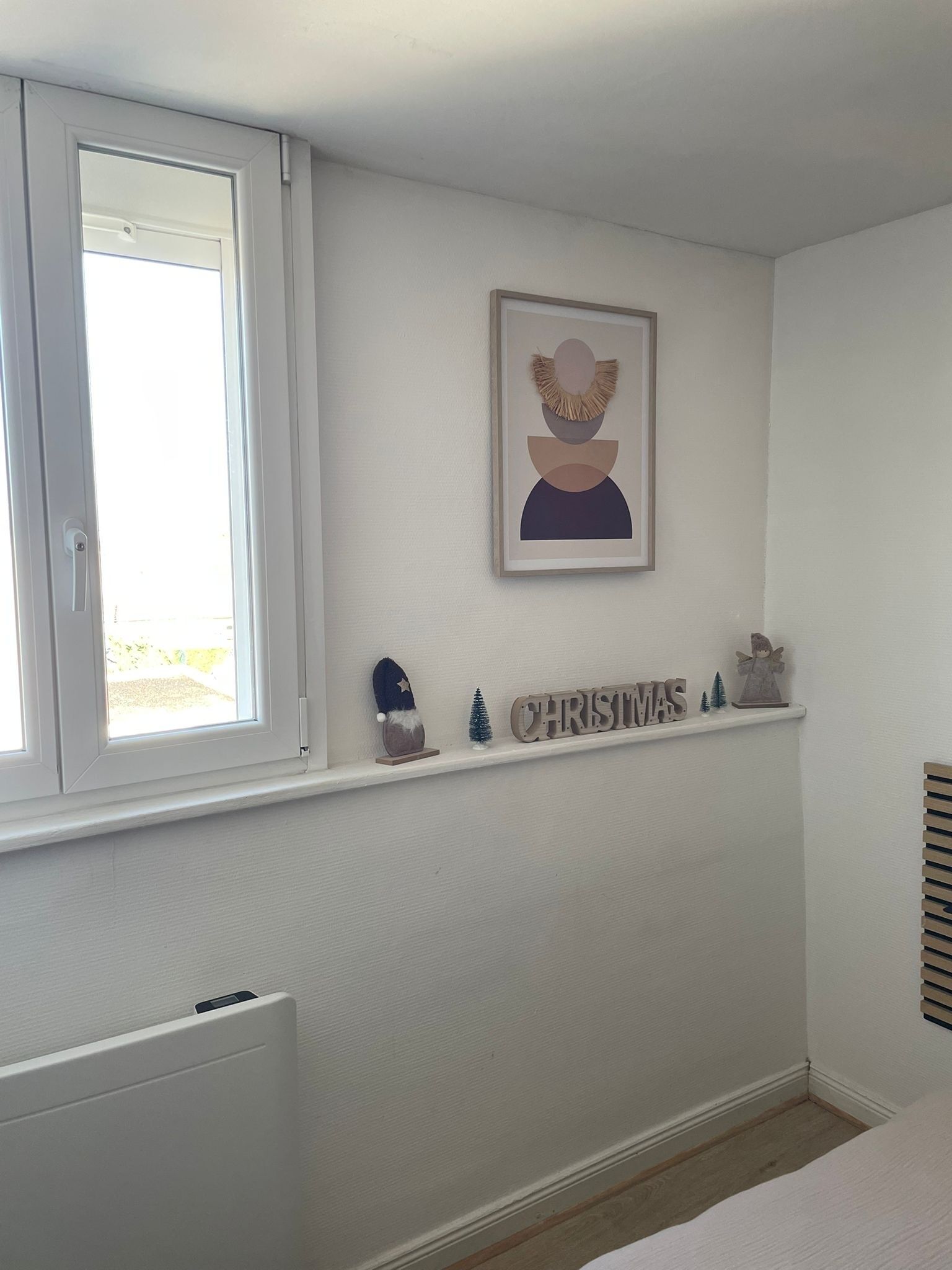 Un dormitorio con ventana, un cuadro enmarcado, una estantería con adornos navideños y un radiador.