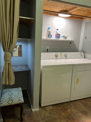 Une buanderie équipée d’un lave-linge, de bouteilles de lessive et d’un petit banc.