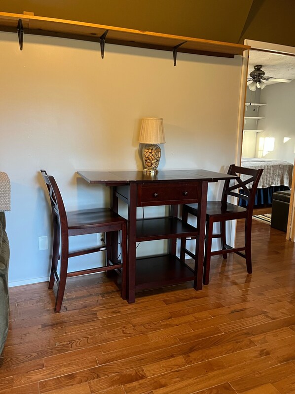 Un coin repas avec une table et des chaises en bois, une lampe avec un pied en liège et un ventilateur de plafond.