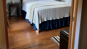 Un dormitorio con piso de madera, una cama con cubrecama blanco y azul, un ventilador de techo y estantes empotrados.