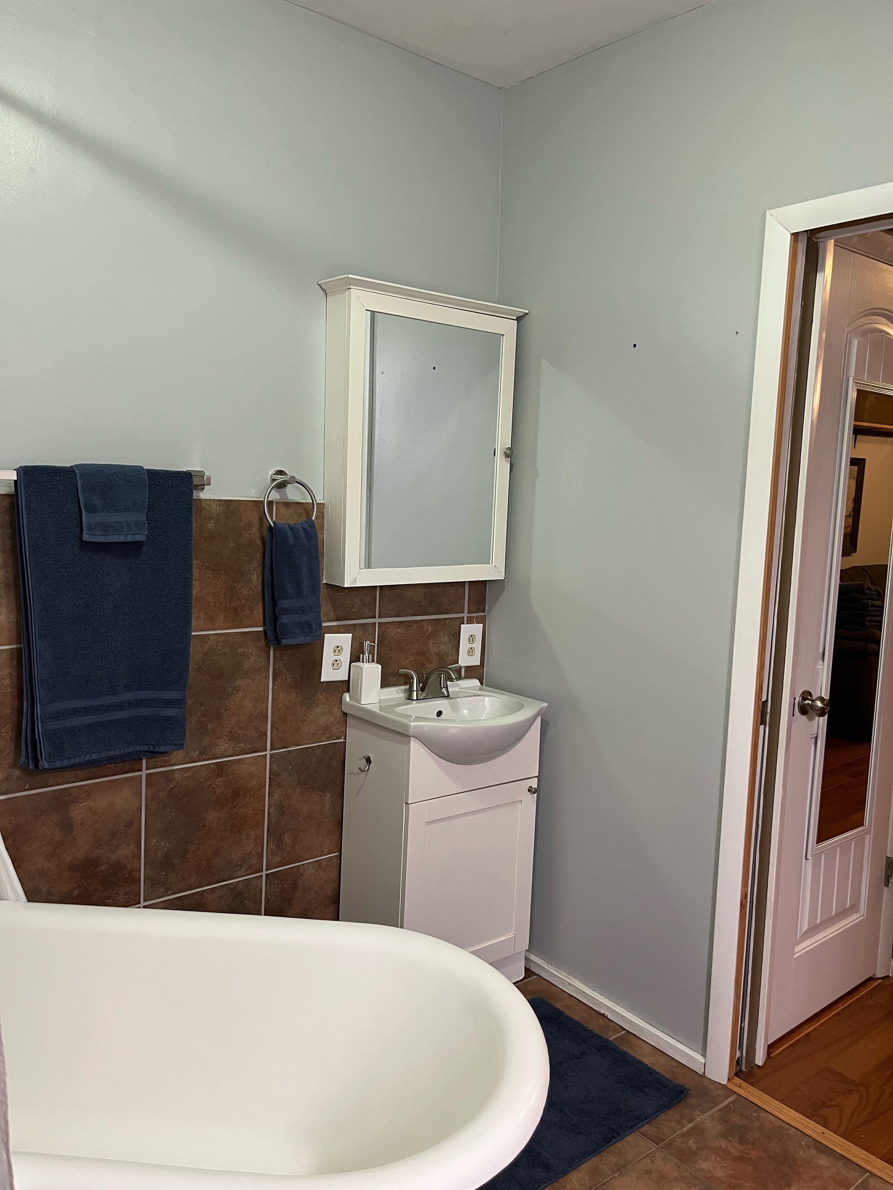 A bathroom with a white bathtub, a white sink, and a mirror above the sink. There are two towels hanging on a rack.