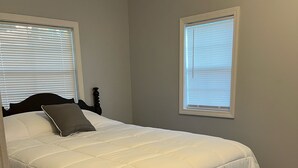 A bedroom with a bed, two windows, and a carpeted floor.