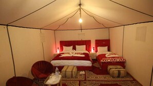 A tent-style room with two beds, a chair, and a small table with a bottle and slippers.