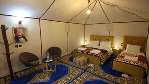 A tent-style room with two beds, a chair, a small table, and a rug.