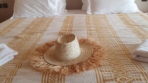 A bed with a patterned bedspread, two white pillows, and a straw hat on the bed.
