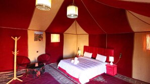 A tent-style room with a bed, two chairs, a table, and a coat rack.
