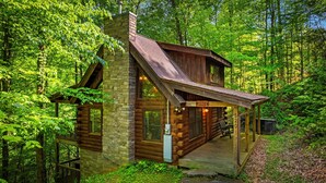 A log cabin with a stone chimney, a porch, and a sign indicating it is a Black Beary Bungalow.